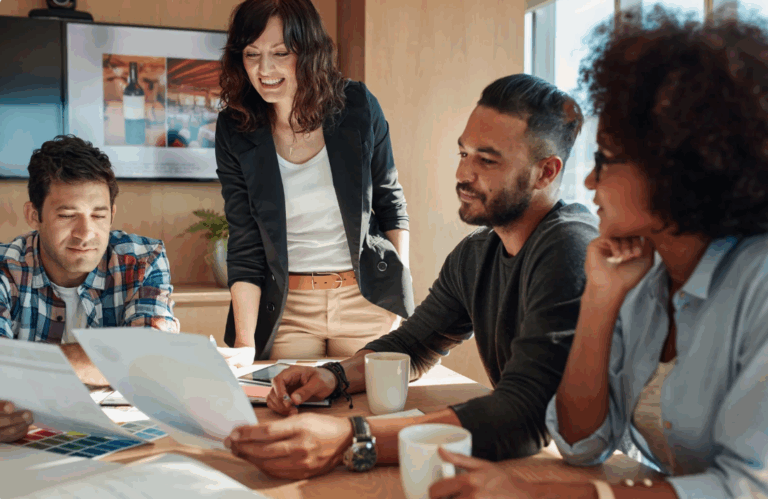 a team gathered around a table looking at a laptop and talking to one another