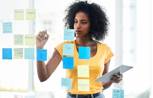 a Black woman looks at ideas on a post it notes on glass